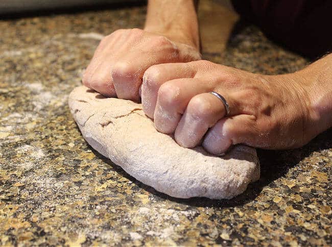 Two hands kneading dough on a granite countertop.