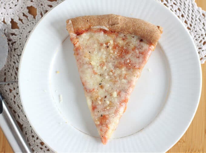 One slice of pizza on a white plate with a doily underneath.