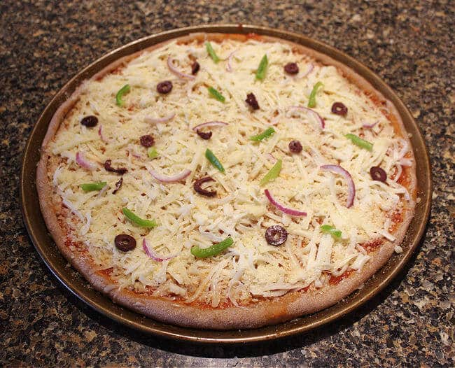 Unbaked pizza on a pizza pan on top of a granite counter. 