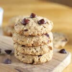 Stack of four chocolate chip cookies on a cutting board.