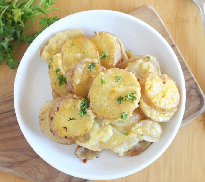 Overhead shot of scalloped potatoes on a white plate with parsley.