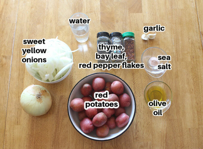 Potatoes, onions, garlic, and spices laid out on a wood table.