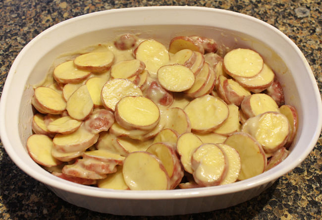 Sliced potatoes and cream sauce in a white casserole dish.