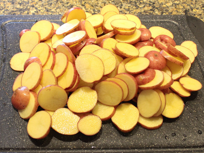 Sliced red potatoes on a black cutting board.