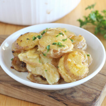 Sliced potatoes in a creamy sauce on a white plate.