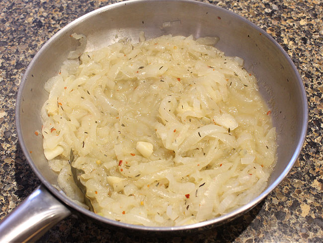 Sauteed onions with garlic and bay leaf in a stainless steel pan.