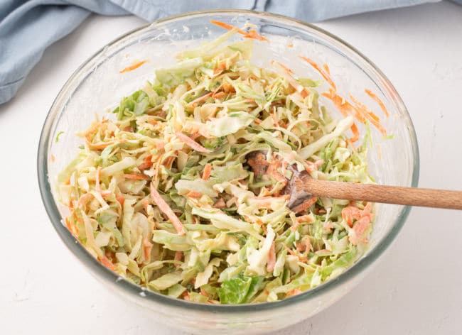 Stirring coleslaw in a clear bowl.