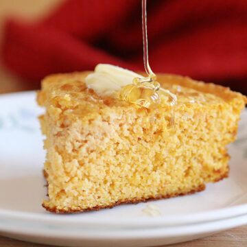 Cornbread on a white plate being drizzled with honey.