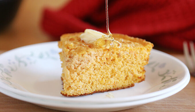 Cornbread on a white plate being drizzled with honey.