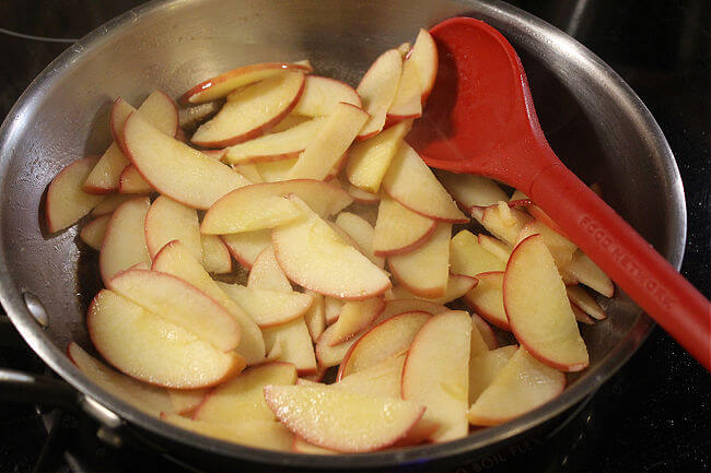 Sliced apples in a steel pan with a red spoon.