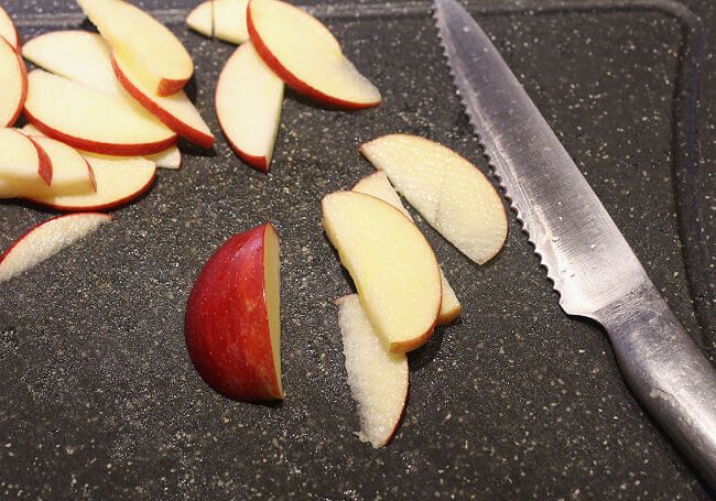 Apple slices and silver knife on a black cutting board.