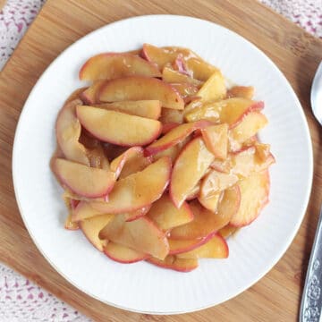 Overhead shot of gooey apple slices on a white plate with a doily and wooden cutting board.