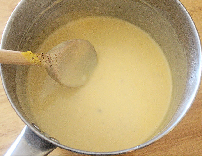 Cheese sauce being stirred with a wood spoon.