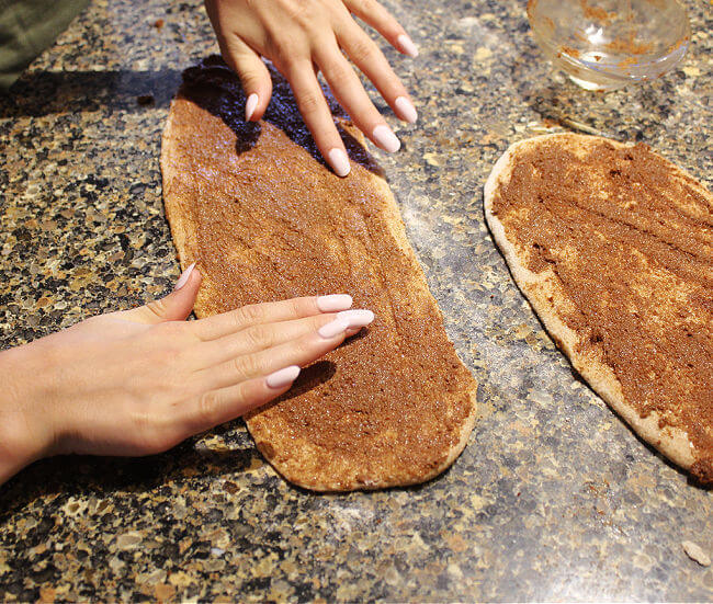 Hands spreading cinnamon sugar mixture onto long pieces of dough.