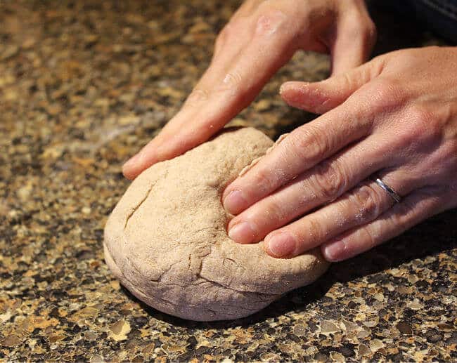 Hands kneading dough on a granite countertop.