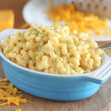 Macaroni and cheese in a small blue baking crock with cheddar cheese around.