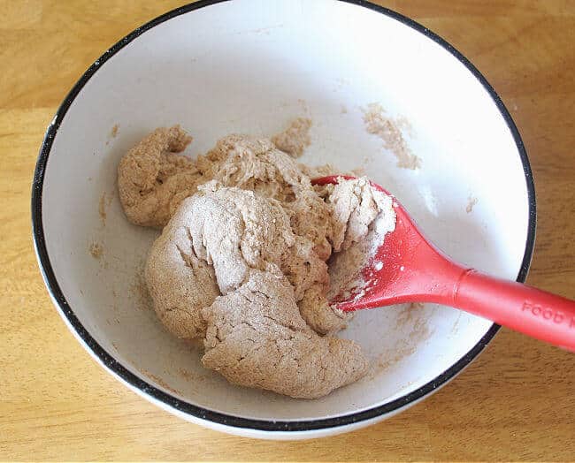 Ball of dough in a white bowl with a red spoon sticking out.