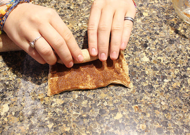Hands rolling up cinnamon rolls on a granite countertop.