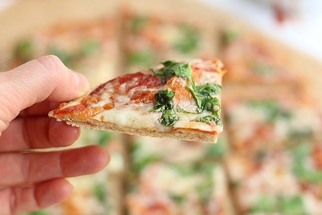 Hand holding a piece of thin crust pizza.