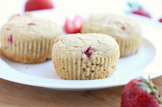 Strawberry muffin on a plate surrounded by strawberries.