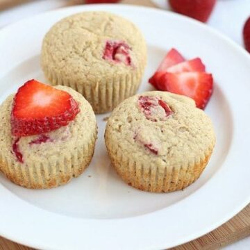 Three muffins and strawberries on a plate.