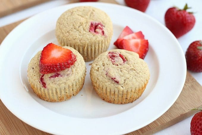 Three muffins and strawberries on a plate.