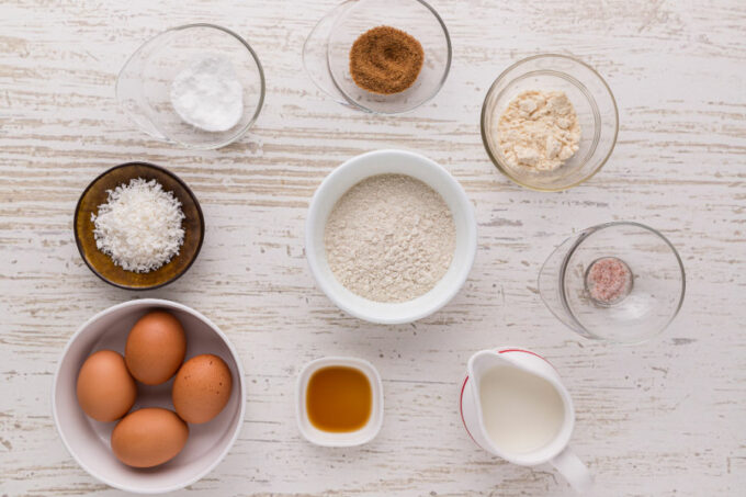 Flour, eggs, milk, and spices laid out in small bowls on a counter.