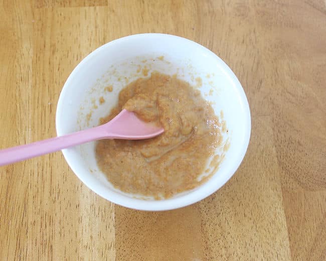 Peanut butter and milk in a bowl being mixed with a pink spoon.