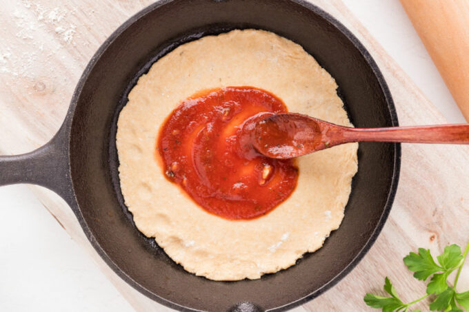 Sauce being spread on an unbaked pizza crust.