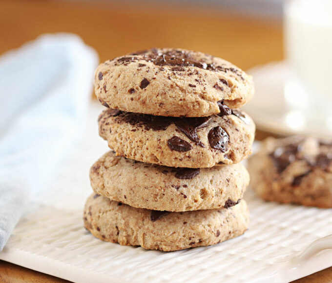 Stack of four chocolate chip cookies on a white plate.