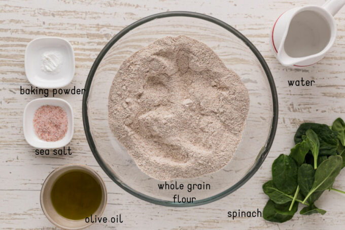 Flour, baking powder, salt, spinach, water, and olive oil laid out on a table.