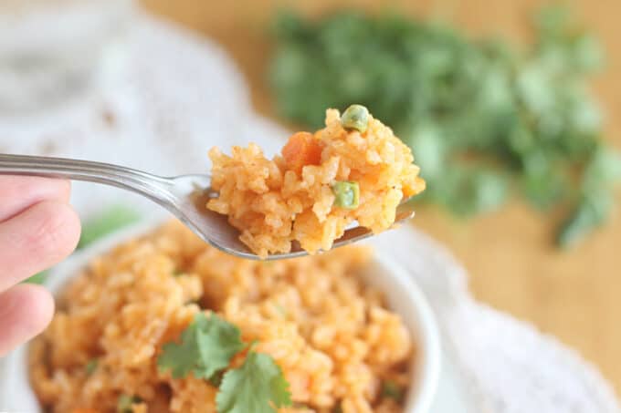 Mexican rice on a fork with cilantro in the background.