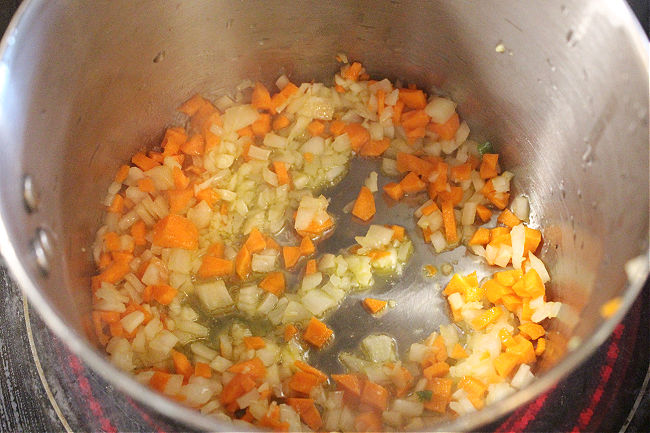 Onion and carrot sauteing in a steel pan.