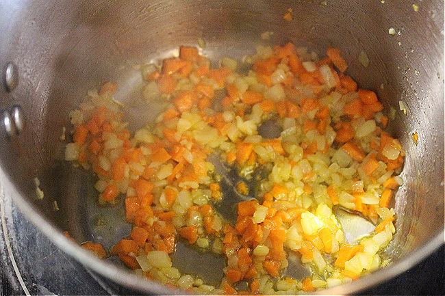 Onion, garlic, and carrot cooking in a steel pot.