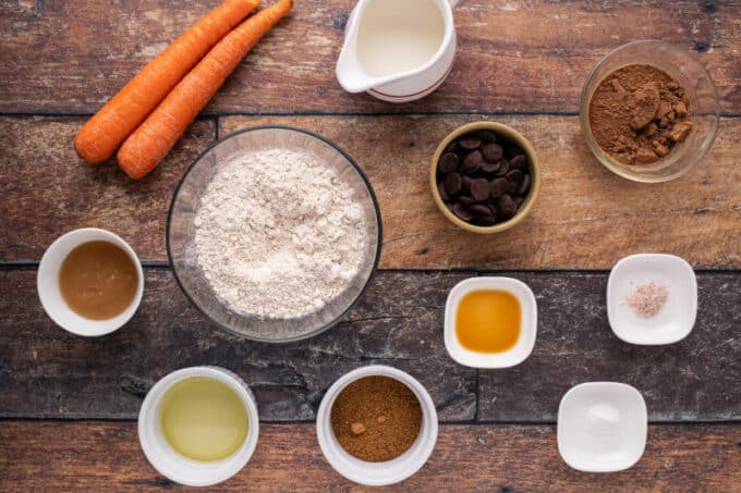Flour, cocoa powder, carrots, and other ingredient laid out on a table.