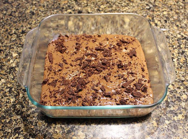 Brownie batter with chocolate chips on top spread out in a baking dish.