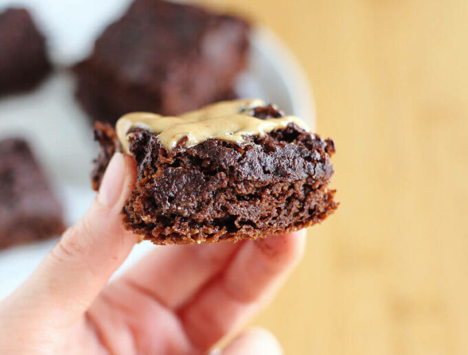 Hand holding a brownie topped with peanut butter.