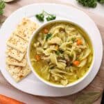 Bowl of chicken noodle soup on a plate with crackers.