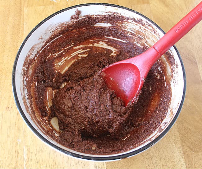 Dark chocolate cookie dough batter being stirred with a red spoon.