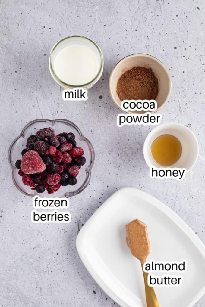 Milk, cocoa, berries, honey, and almond butter laid out on a table.