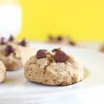 Chocolate chip cookie on a white plate with a yellow background.