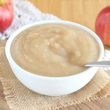 White bowl filled with applesauce on a wood cutting board.