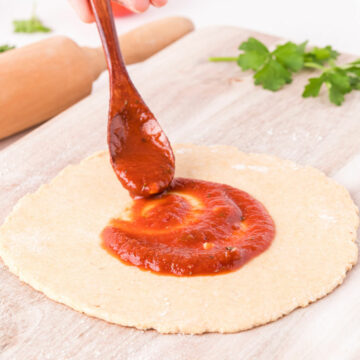 Pizza sauce being spread on pizza dough.