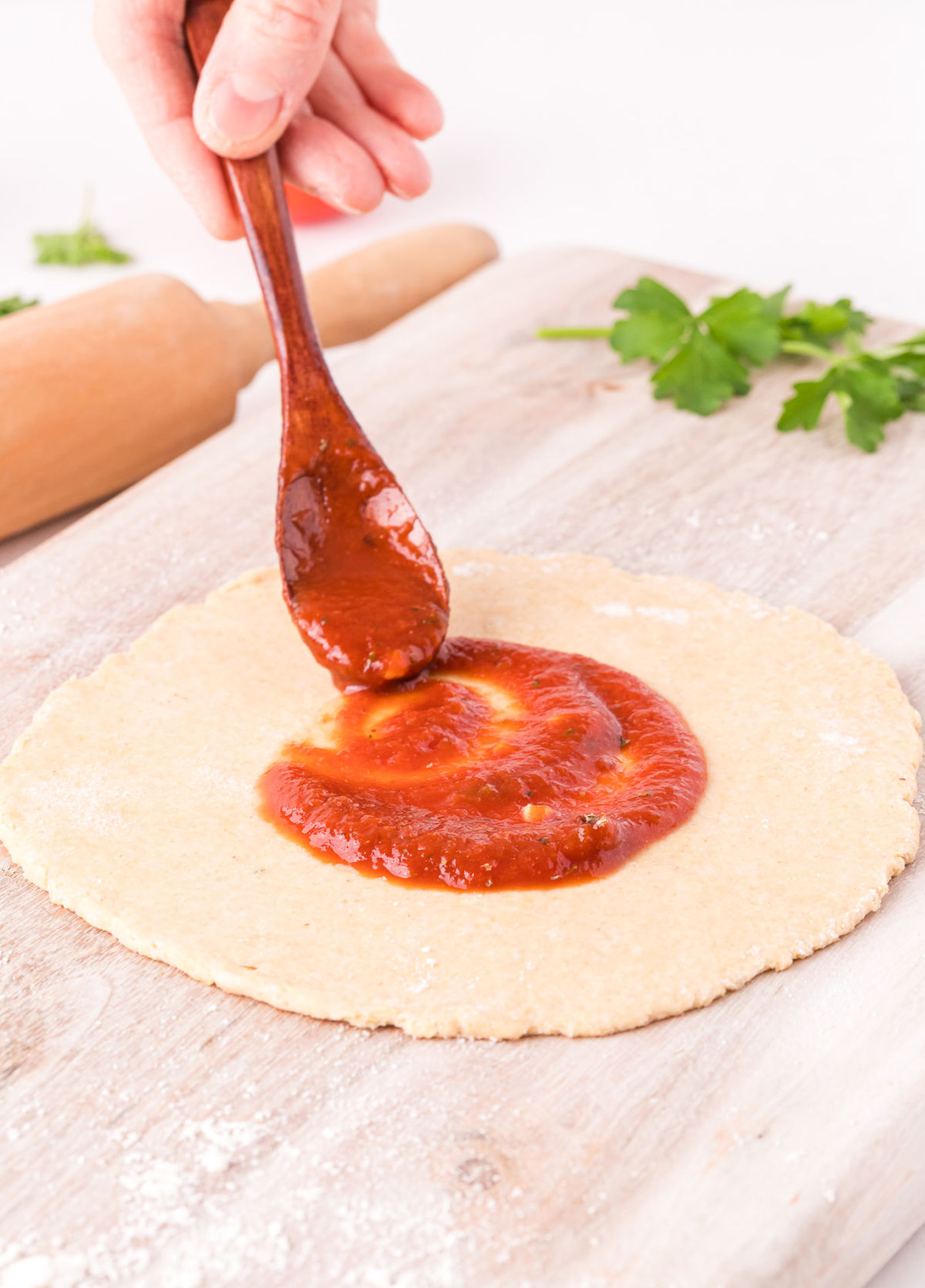 Pizza sauce being spread on pizza dough.