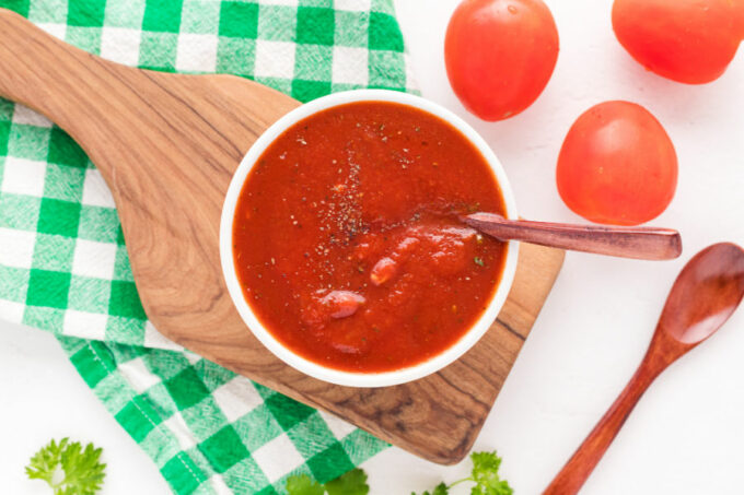 Bowl of pizza sauce on a cutting board.