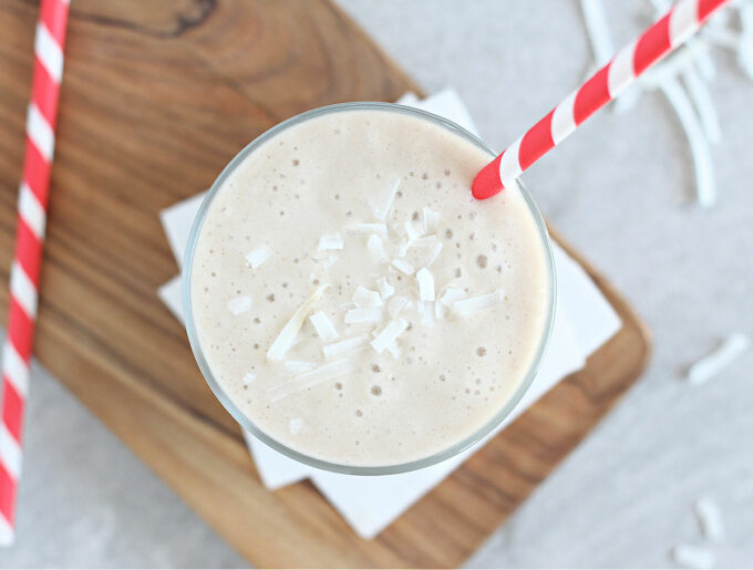 Top down view of a white milkshake in a glass sitting on a wood cutting board.