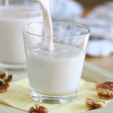 Milk being poured into a glass surrounded by walnuts.