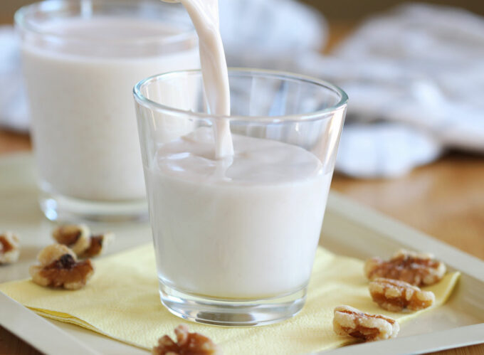 Milk being poured into a glass surrounded by walnuts.