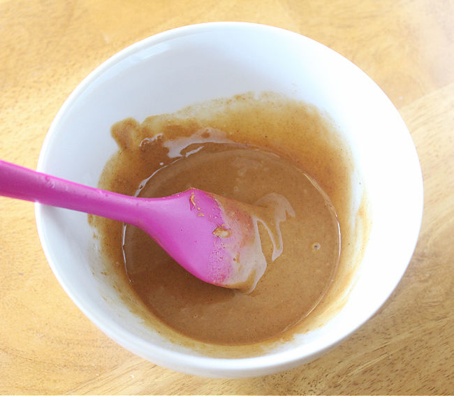Peanut butter and coconut oil being stirred in a bowl with a spatula.