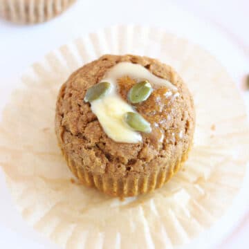 Pumpkin muffin on a wrapper with butter and pumpkin seeds on top.